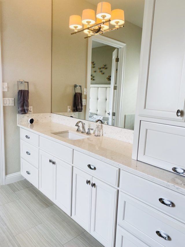 A long white double vanity with a chandelier reflected in the mirror above it