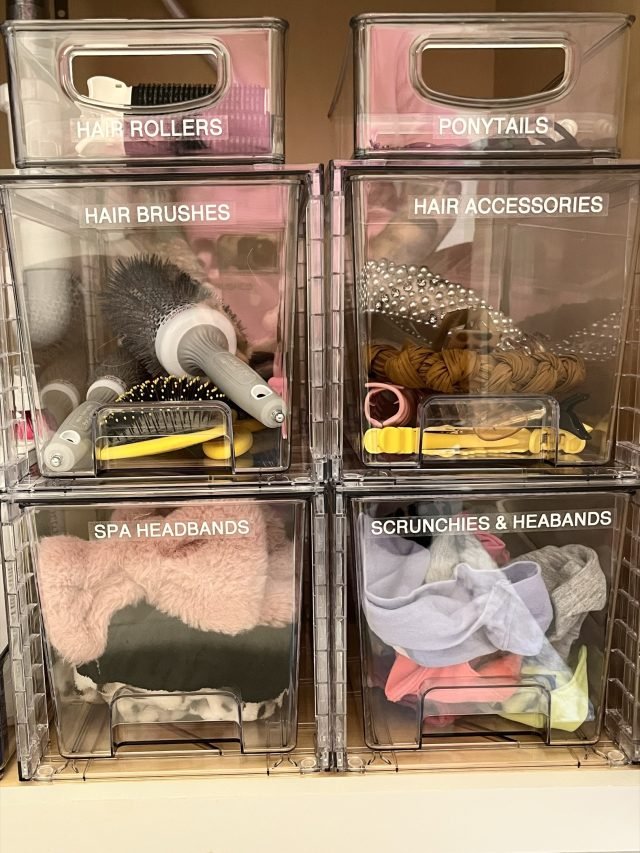 Stacked clear bins labeled hair rollers, ponytails, brushes and headbands