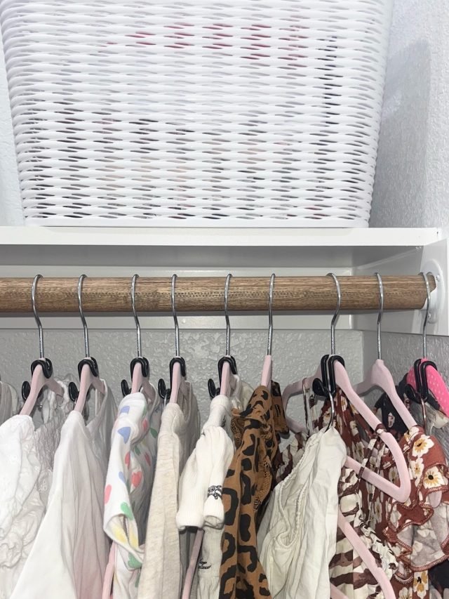 A closet rod of light garments beneath woven storage baskets on the shelf above