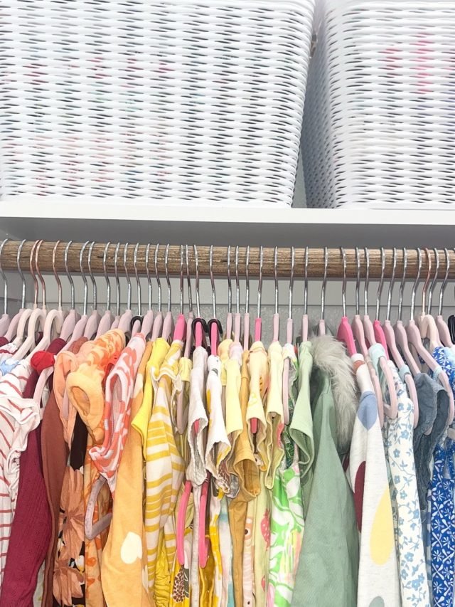 Children's clothes hung on pink hangers with woven baskets stored above