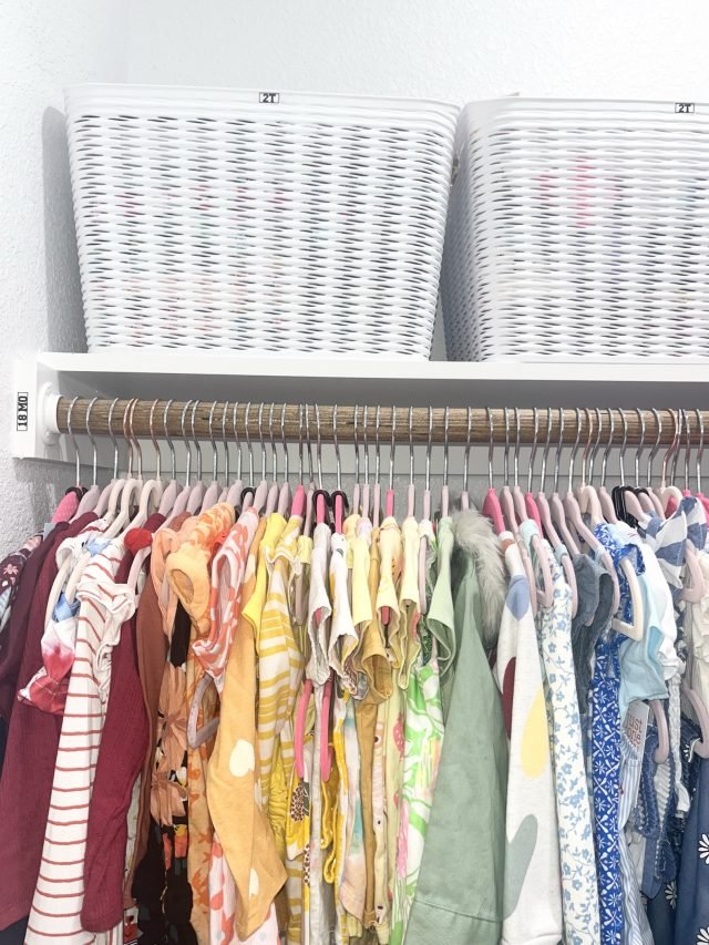 White woven baskets on an upper shelf above a row of hanging patterned clothing