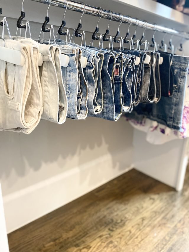 Denim hung by style on matching hangers along a reach-in closet rod