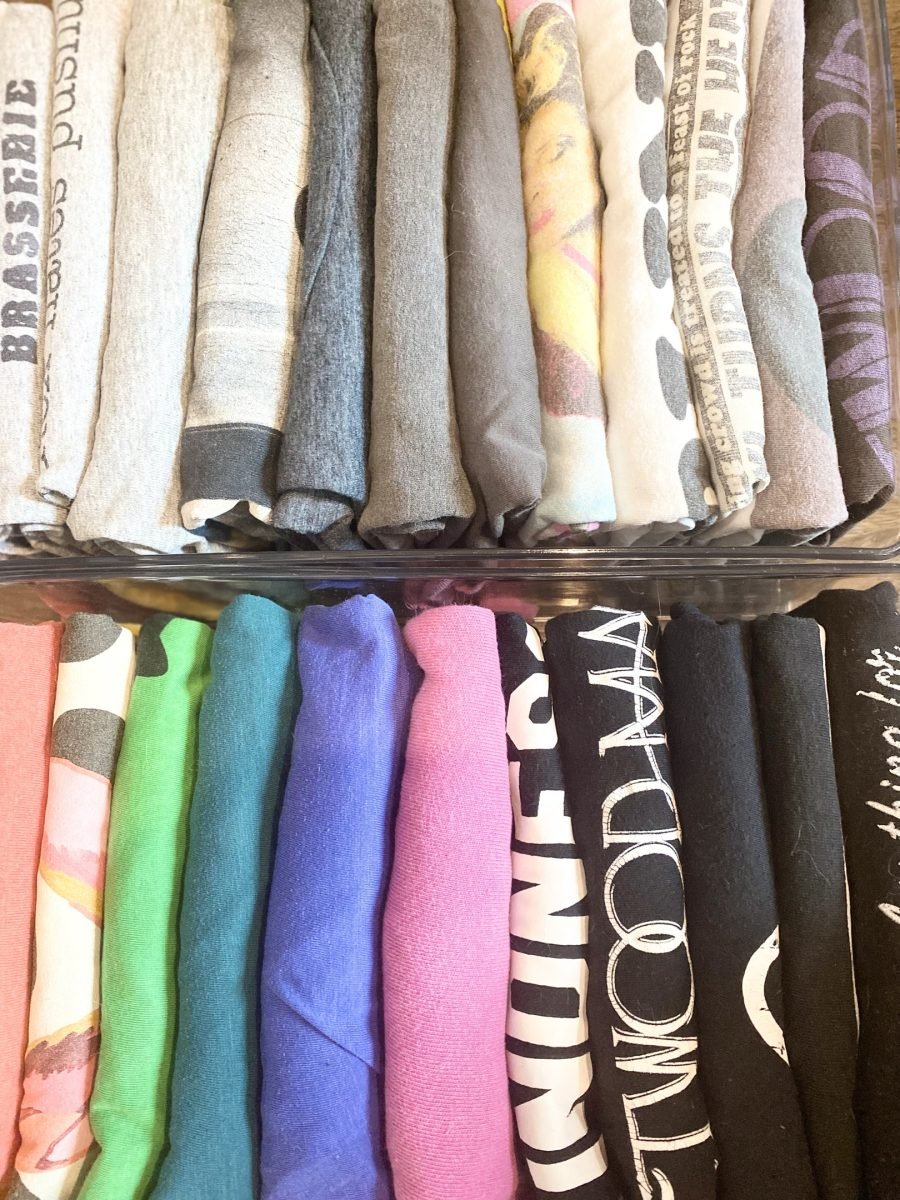 Folded sweaters and printed T-shirts stacked by color on a closet shelf