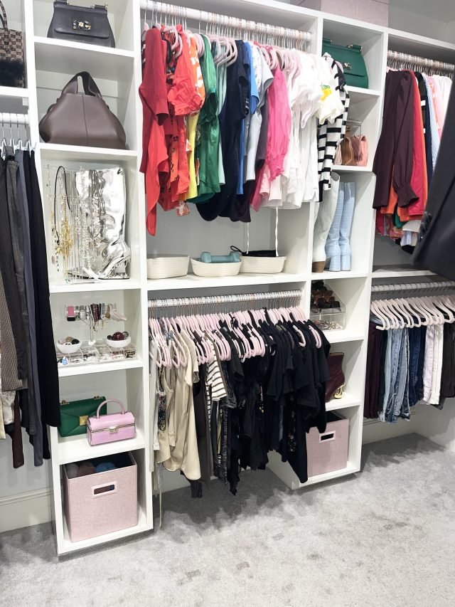 A corner walk-in with hanging rods, open shelving and labeled fabric bins