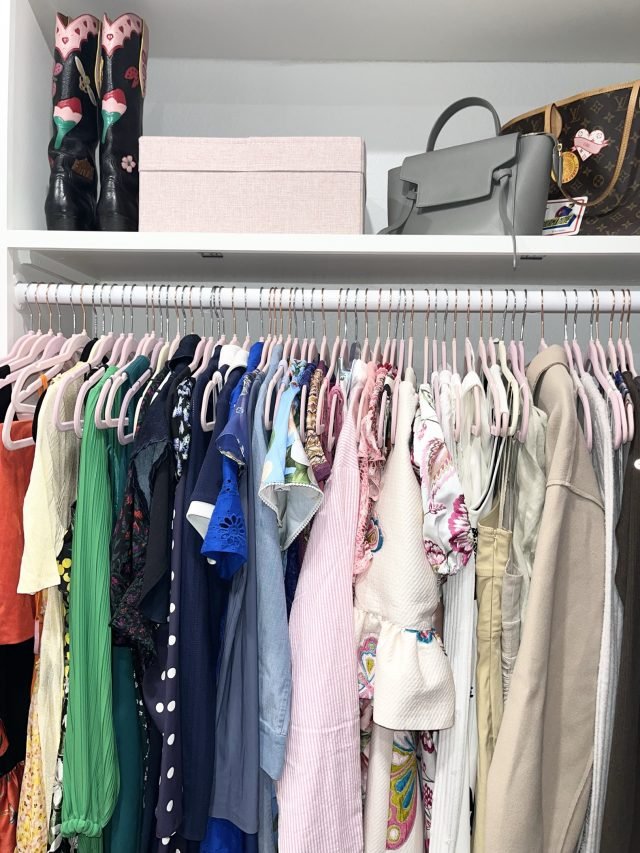 Handbags and a hat box shelved above a long rod of colorful dresses