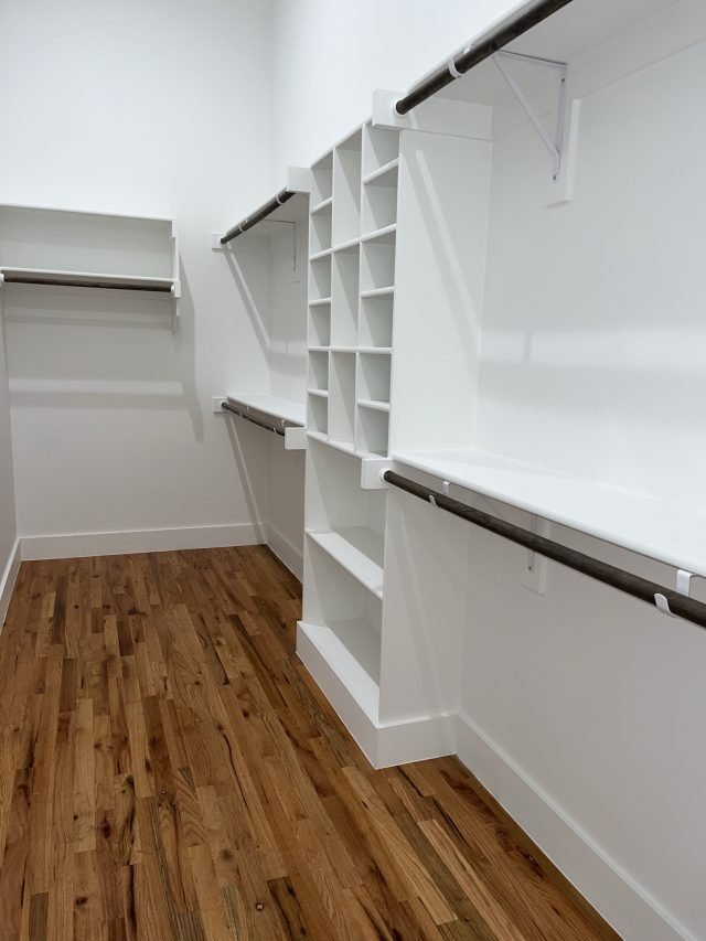 An empty white walk-in closet with new shelving and a wooden floor