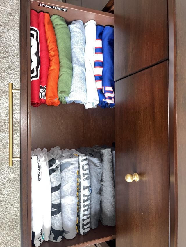 A teen's closet with rolled tees above and folded athletic shorts below