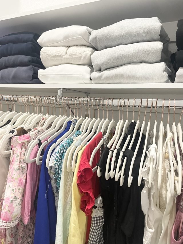 Folded sweaters and white towels above a row of hanging blouses on matching hangers