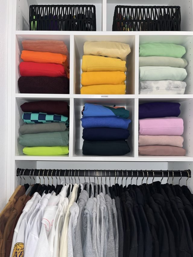 A grid of cubbies holding folded clothes by color above a hanging rod