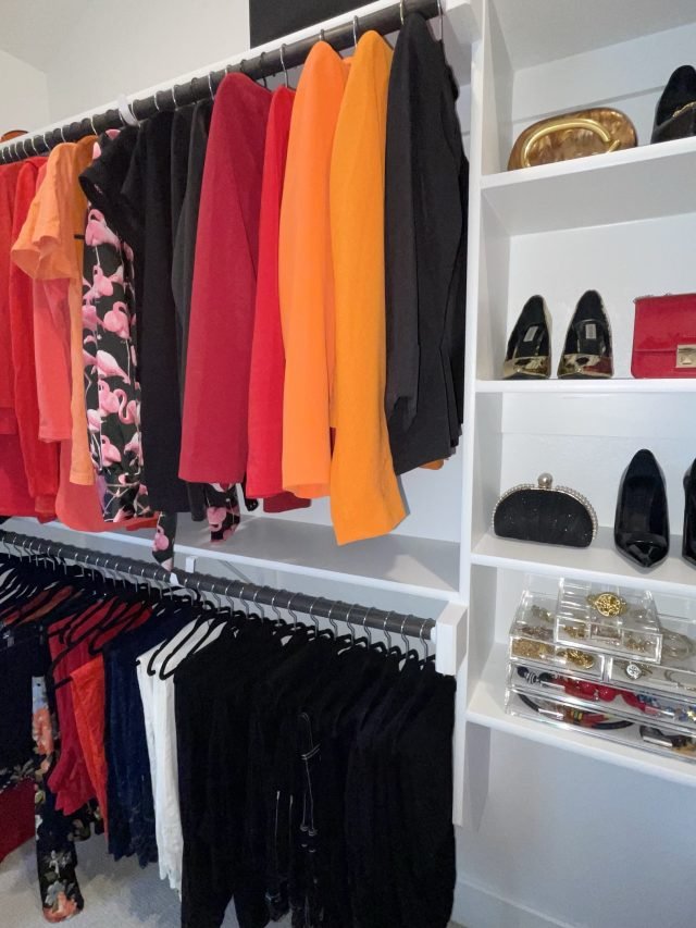 A bright walk-in with tops sorted by color above and black pants below