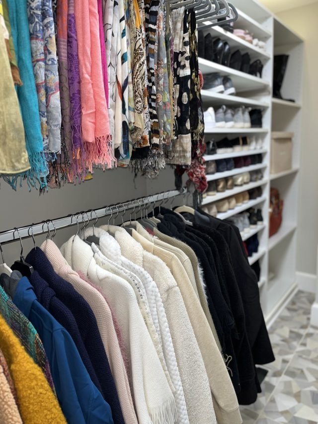 Scarves hung along a rod above coats sorted light to dark