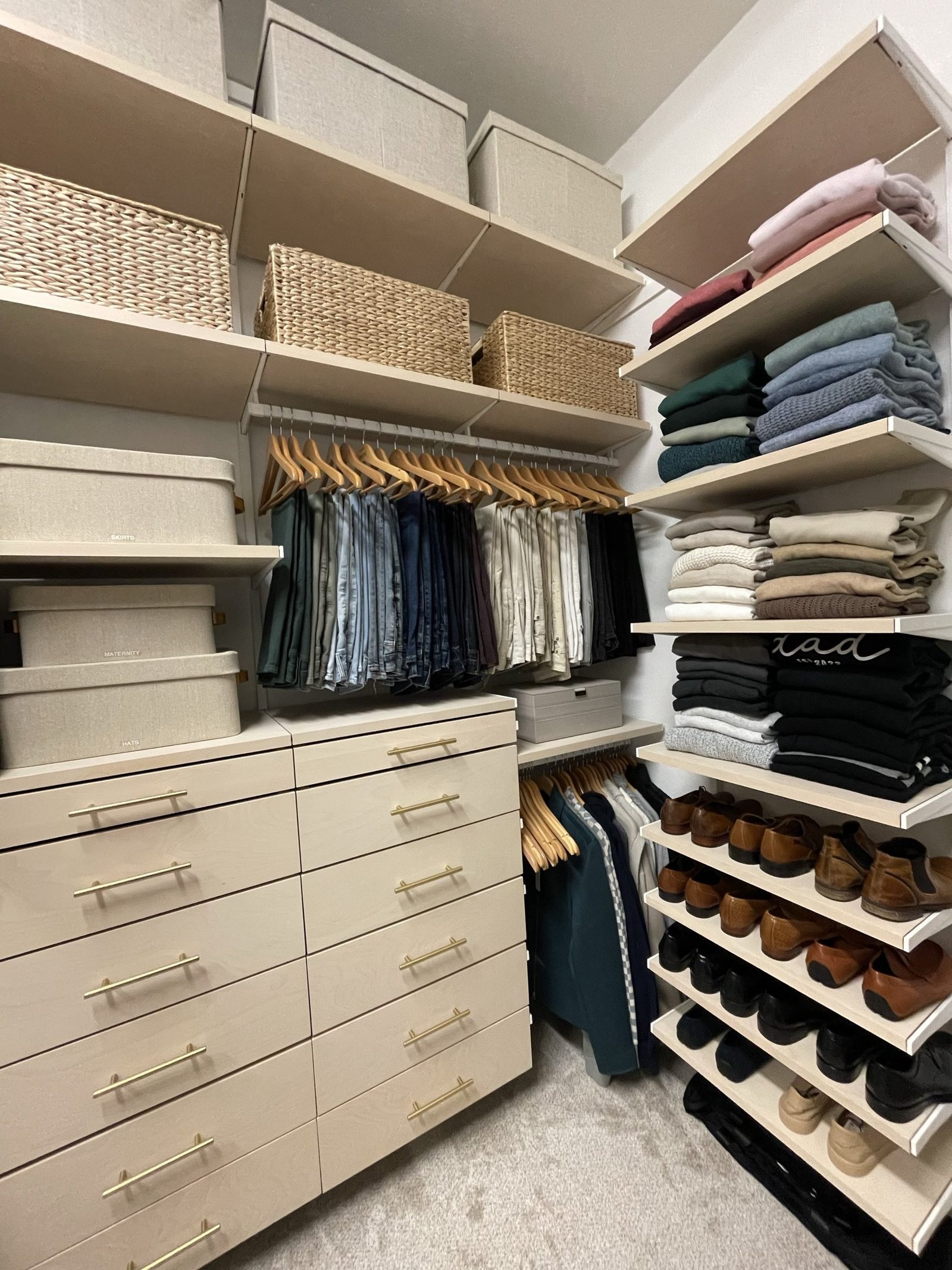 A finished walk-in closet with a bank of drawers, hanging sections either side and shoes shelved at floor level
