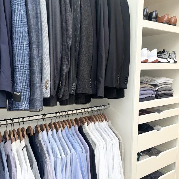 A men's closet with suits above, dress shirts below and shoes shelved