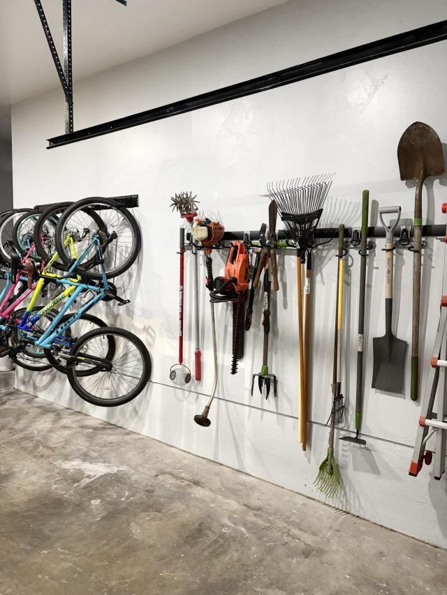 Garden tools and bikes hung on a garage wall track to clear the floor