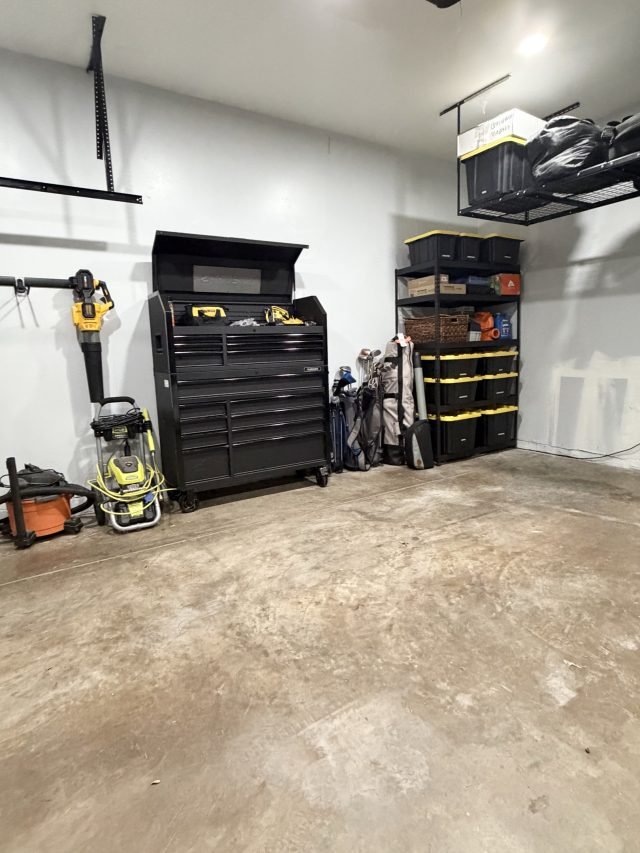 A garage with overhead racks, a tool chest and shelved bins along one wall