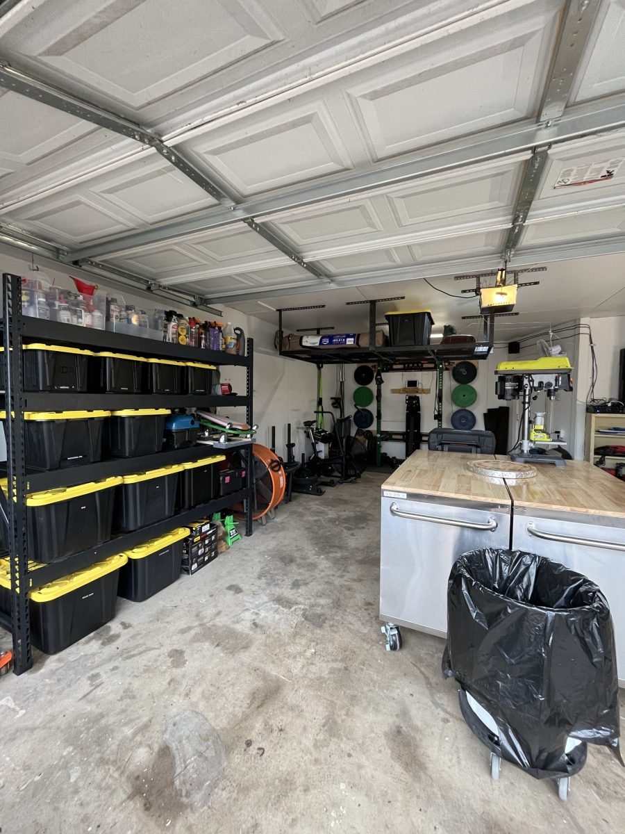 A cleared garage with labeled totes on wall racking and a work surface