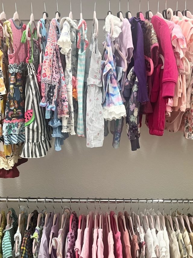 A nursery closet with dresses hung above and sleepers below by color
