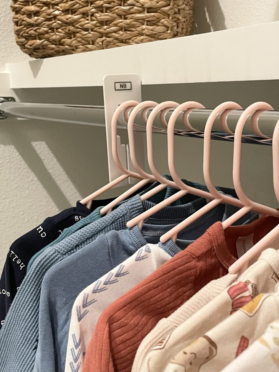 Baby clothes on pink hangers beneath a labeled size divider