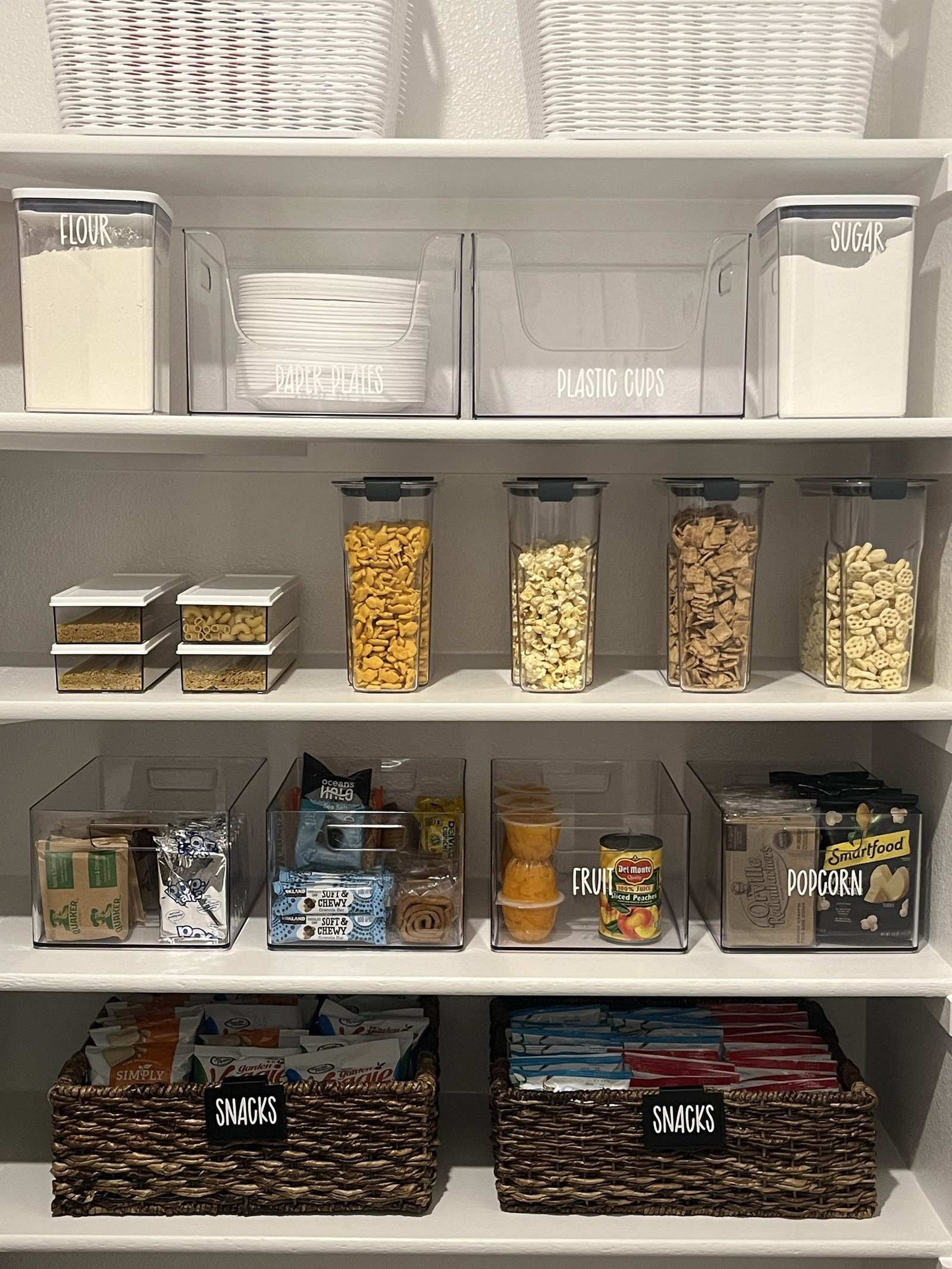 A pantry with clear bins on white shelving and baskets holding everyday staples