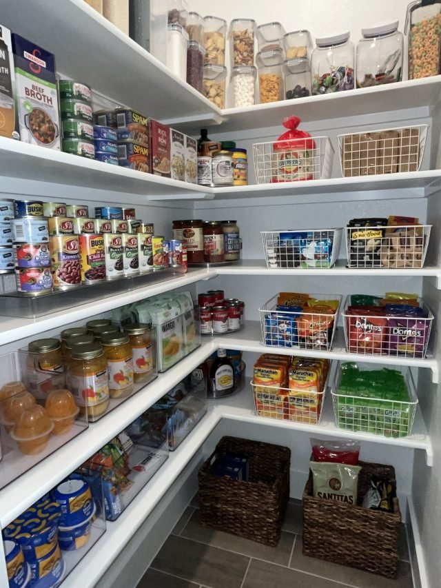 A corner pantry with canned goods, clear bins and woven baskets on every shelf