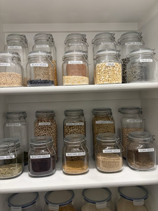 Glass jars of grains and beans labeled on the lid and shelved in rows