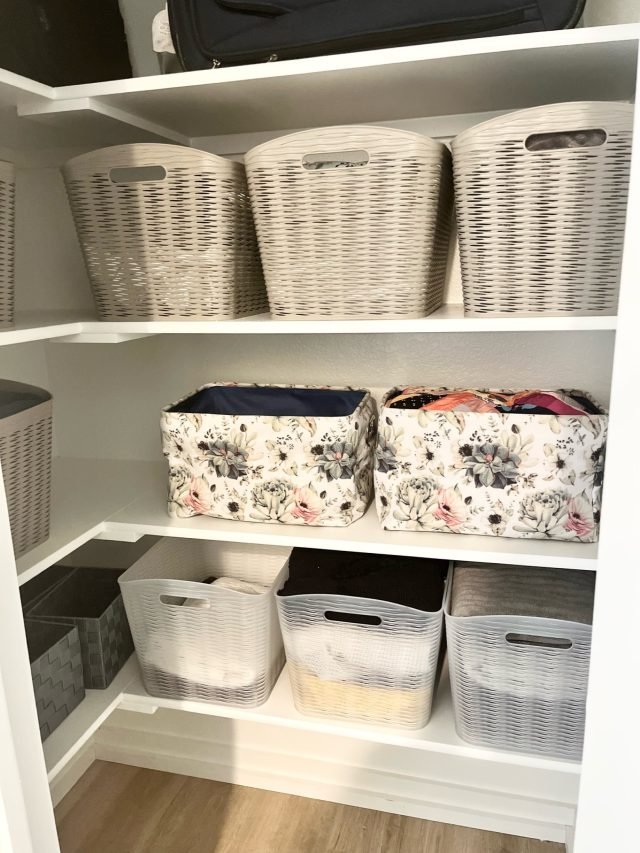 A linen cabinet with woven baskets above and clear bins on the lower shelf