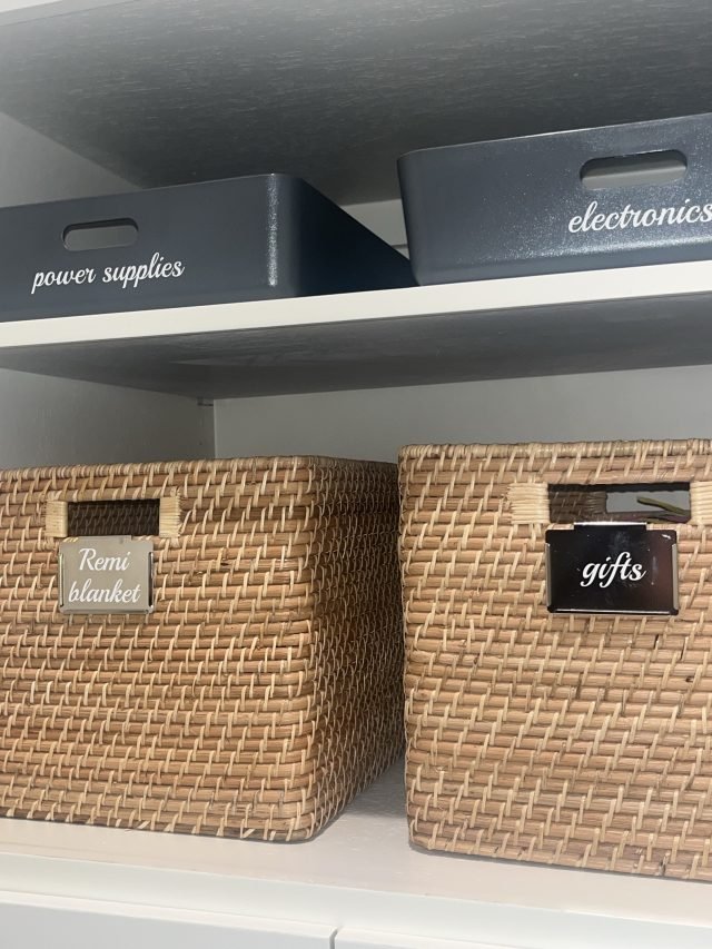 Shelf bins labeled power supplies and electronics beside baskets for gifts and blankets