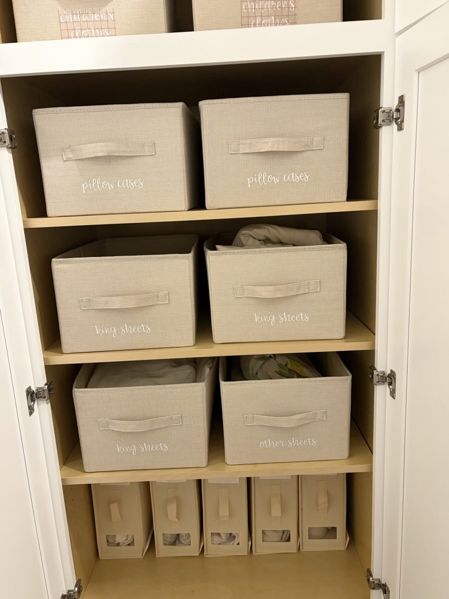 A linen cabinet with fabric bins labeled pillow cases, long sheets and king sheets