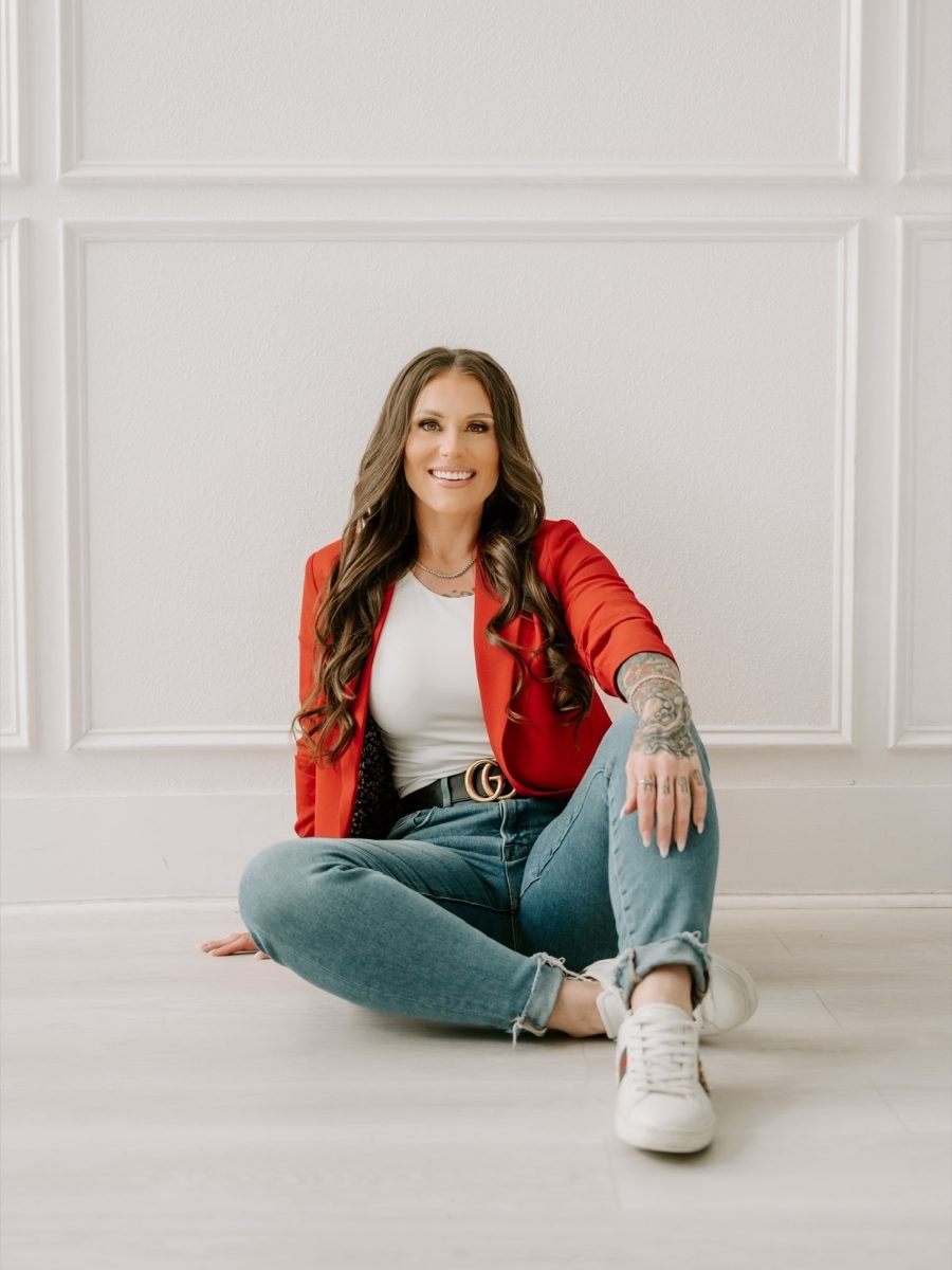 Ashley Matteson seated on the floor in a red blazer and sneakers